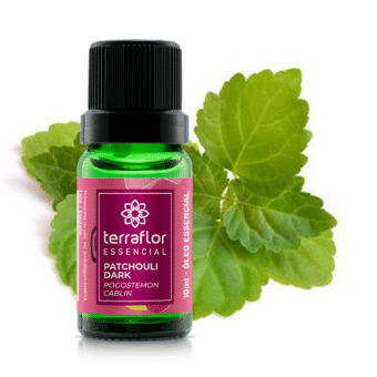 Frasco do óleo essencial de patchouli dark com folhas de patchouli ao fundo.