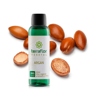 Frasco do óleo vegetal de argan com sementes ao fundo.